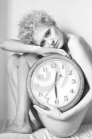 chica-joven-hermosa-con-el-pelo-rizado-que-se-sienta-en-la-cama-con-un-reloj-grande-en-sus-ma...webp