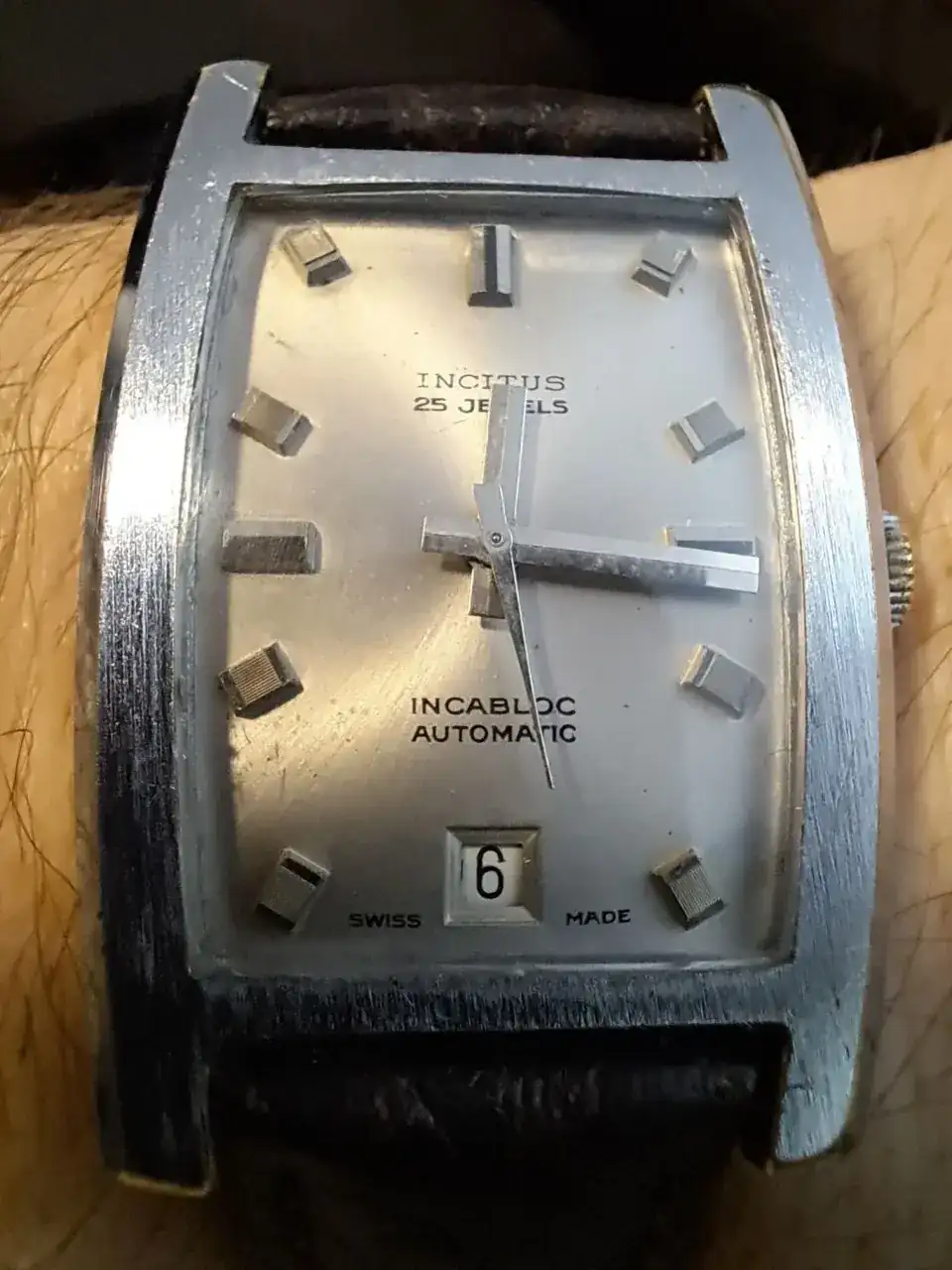 Esfera del reloj, es rectangular y plateada, tanto la caja como la esfera.Muestra el texto Incitus, 25 Jewels, Incabloc (sistema antigolpes de la época), Automatic y Swiss Made.En la parte inferior muestra el número de día del mes.La esfera, en lugar de números, tiene una serie de protuberancias plateadas rectangulares.Parece acero, pero yo diría que es latón con una cobertura plateada.